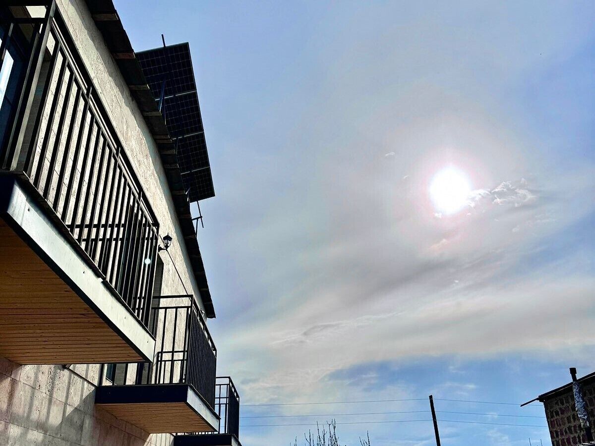 A building with a balcony, a solar panel, and a clear sky with the sun.