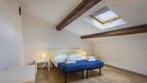 A bedroom with a skylight, a bed with white linens, a bedside table with a lamp, and a wooden floor.
