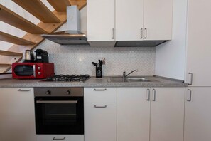 A kitchen with white cabinets, a red microwave, a gas stove, a sink, and a wooden ceiling. - San Zanobi panoramic terrace by MMega (Florence)