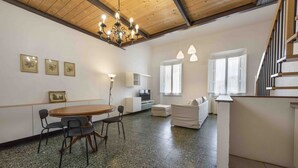 A spacious room with a wooden ceiling, a dining table with chairs, a sofa, and a staircase.