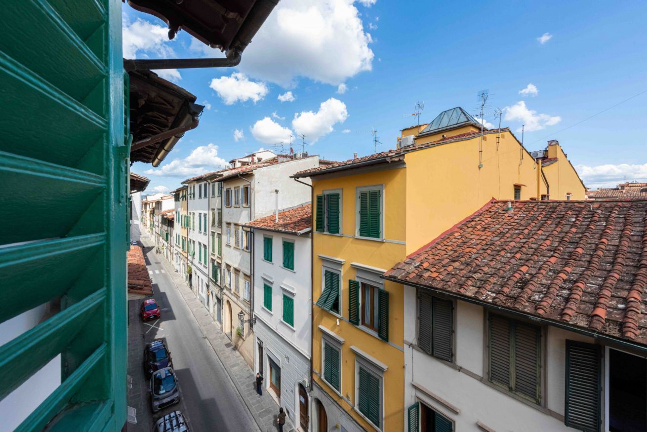 A narrow street lined with multi-story buildings, some with green shutters, under a clear sky.
