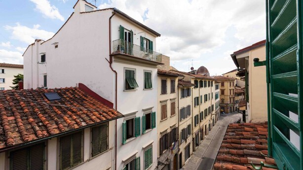 A narrow street lined with traditional buildings, featuring balconies and terracotta roofs.