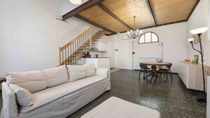 A living room with a sofa, a dining table, and a staircase leading to a kitchen.