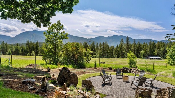 A patio with outdoor seating, surrounded by rocks and trees, with a mountain view in the background. - A serene, rustic farmhouse nestled on the banks of the Jocko River. Perfect for nature lovers, this cozy getaway offers peace, privacy, and stunning outdoor spaces to immerse yourself in the beauty of Montana. (Arlee)