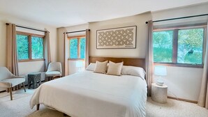 A spacious bedroom with a large bed, two bedside tables with lamps, a chair, and a window with curtains. - A serene, rustic farmhouse nestled on the banks of the Jocko River. Perfect for nature lovers, this cozy getaway offers peace, privacy, and stunning outdoor spaces to immerse yourself in the beauty of Montana. (Arlee)