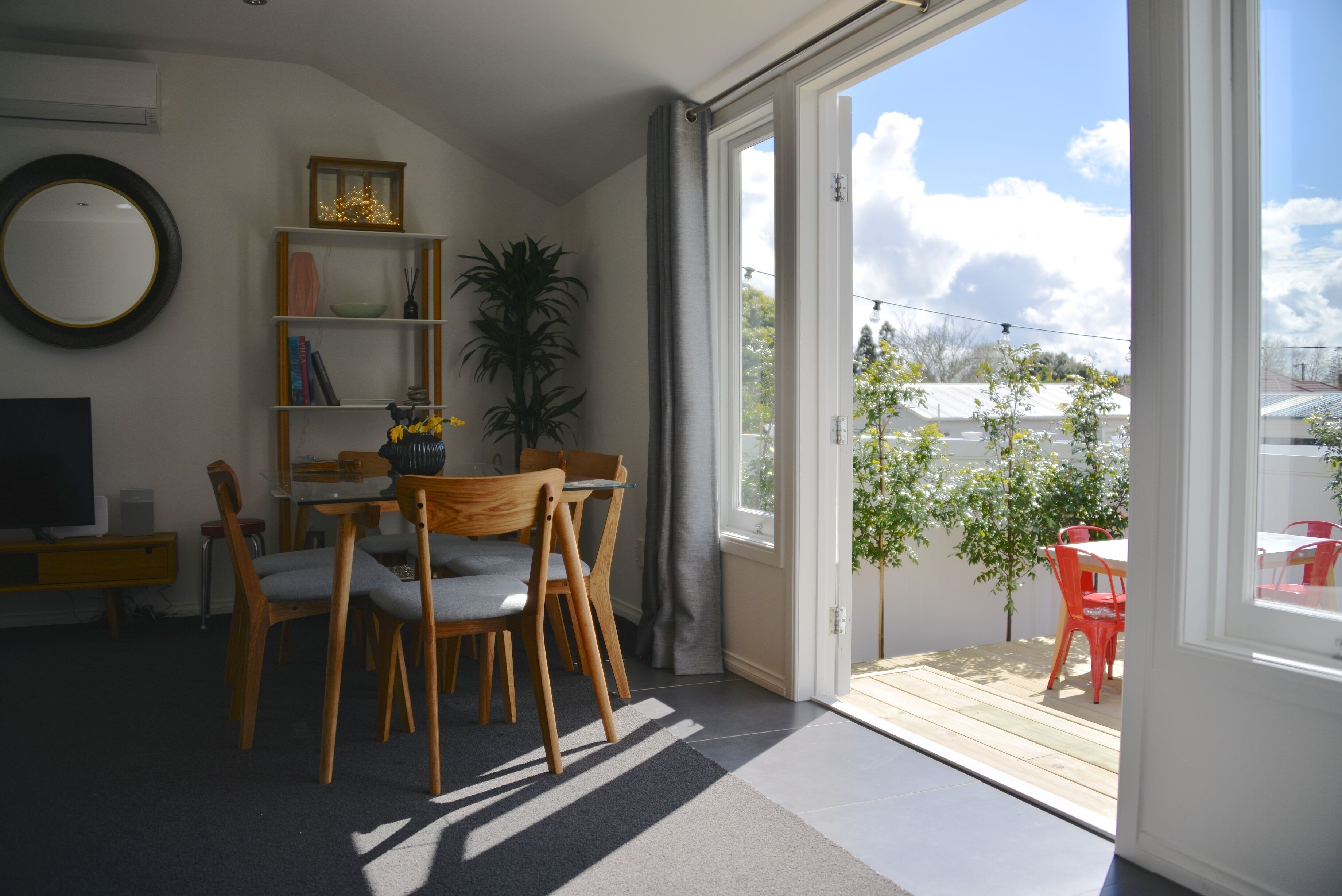 A living room with a dining area, a TV, a bookshelf, and a view of the outdoors.