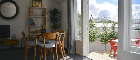 A living room with a dining area, a TV, a bookshelf, and a view of the outdoors.