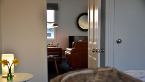 Ein Hotelzimmer mit Bett, Fernseher, Stuhl, Tisch mit Lampe und einer Blumenvase.