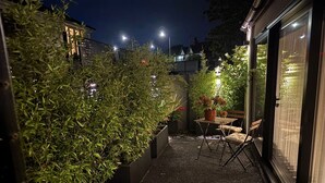 En uteplats med ett bord och stolar, omgiven av krukväxter och en byggnad med stora fönster.
