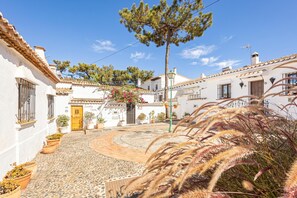 A courtyard with white buildings, a central tree, and potted plants. - La Casita De Pueblo Andaluz (Marbella)
