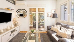 A living room with a flat-screen TV, a glass coffee table, a leather sofa, and a large window with a view of the outdoors. - La Casita De Pueblo Andaluz (Marbella)