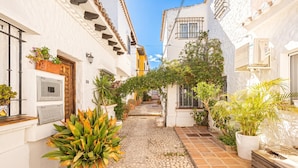 A narrow alleyway with white buildings, potted plants, and a tiled pathway. - La Casita De Pueblo Andaluz (Marbella)