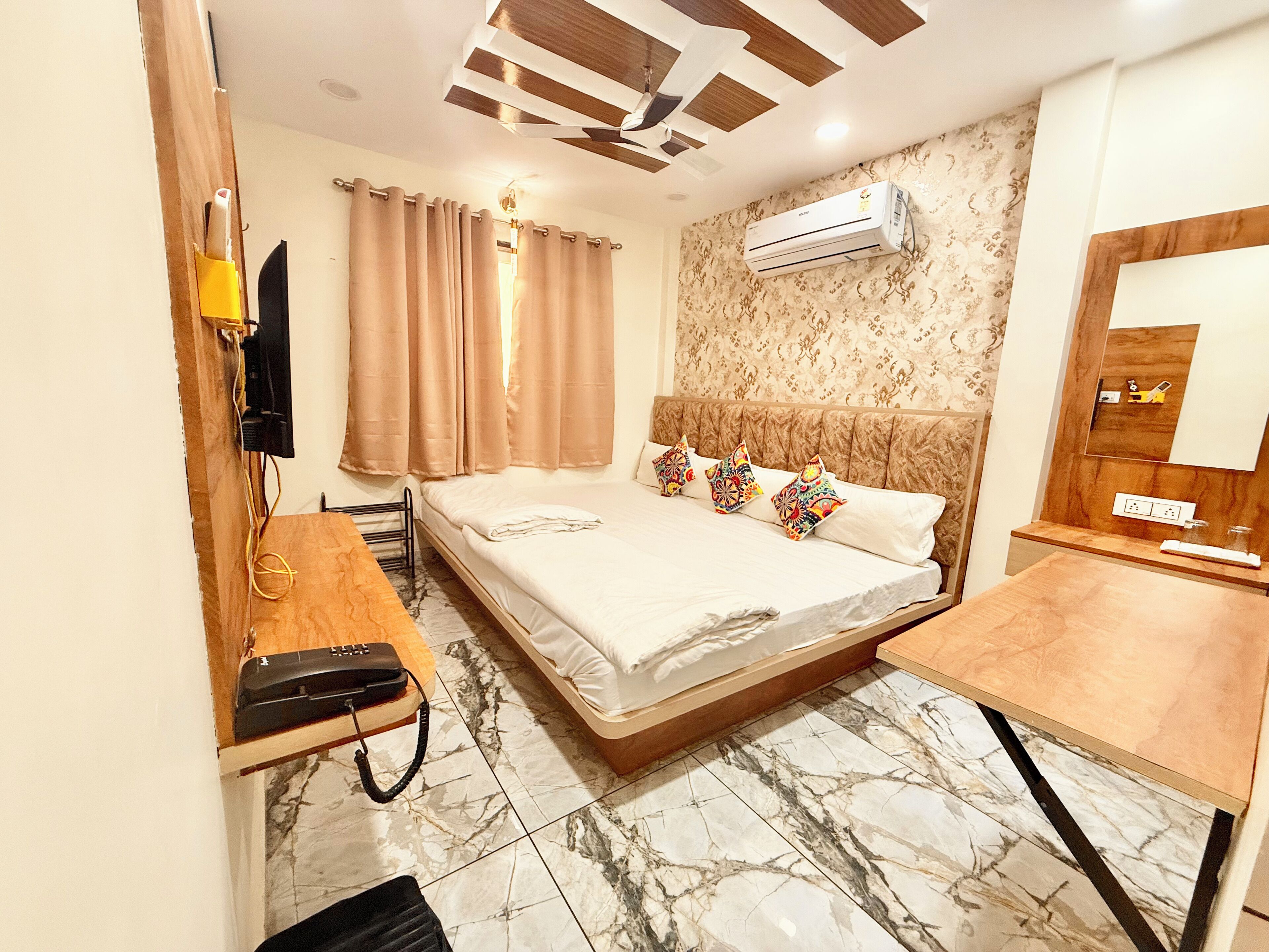 A hotel room with a bed, a desk, a telephone, an air conditioning unit, and a mirror.