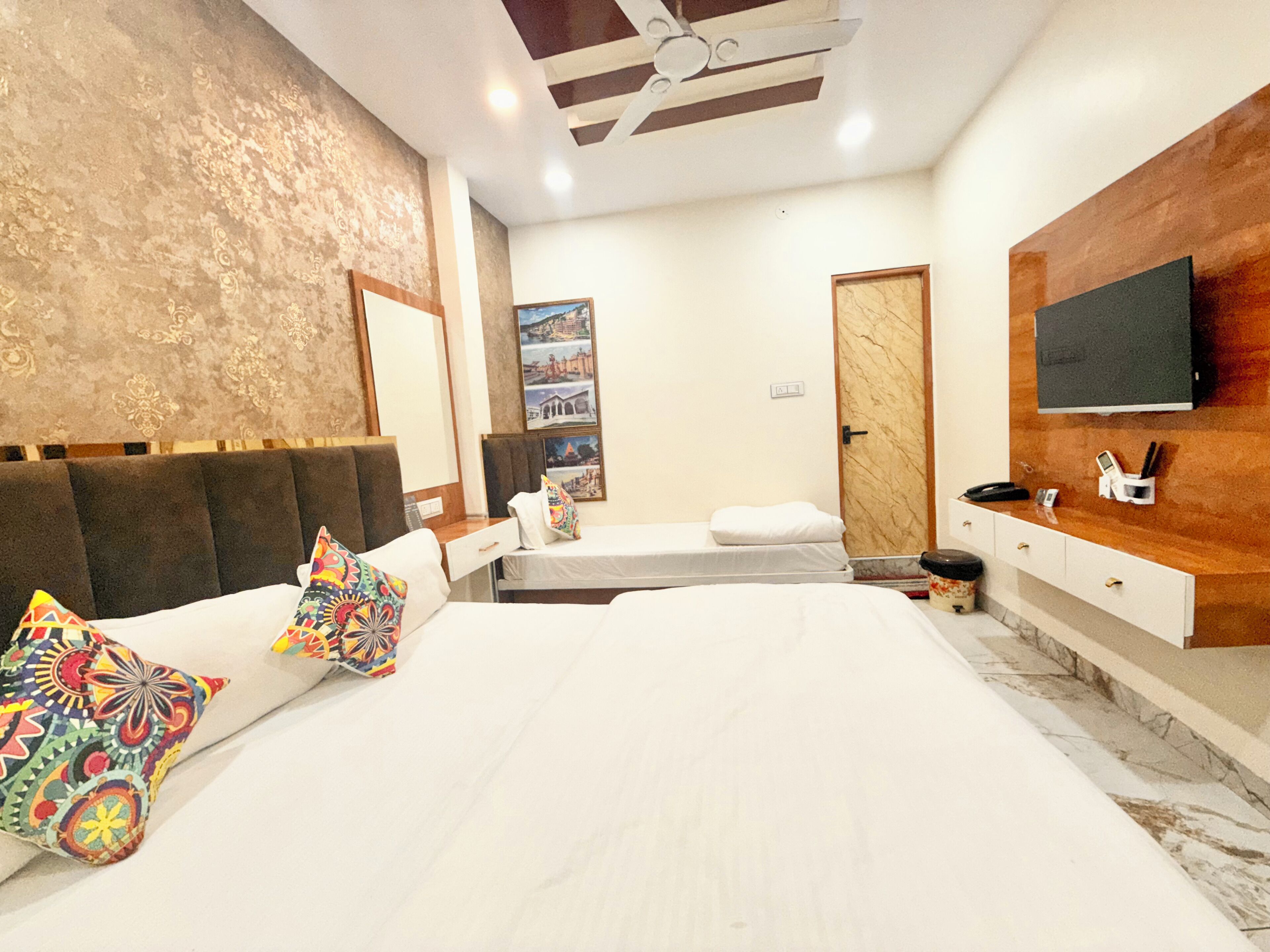 A bedroom with a large bed, a TV mounted on the wall, a ceiling fan, and a marble floor.