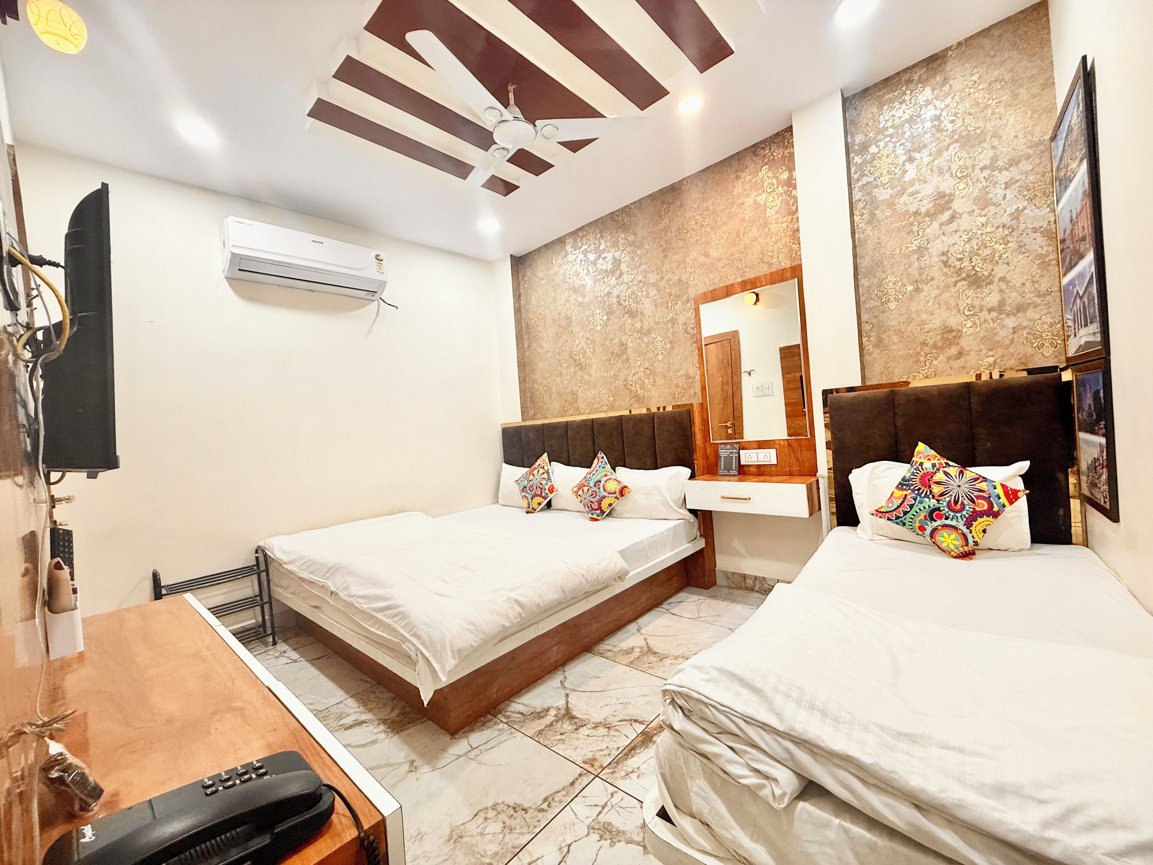 A hotel room with two beds, a desk with a telephone, an air conditioner, and a ceiling fan.