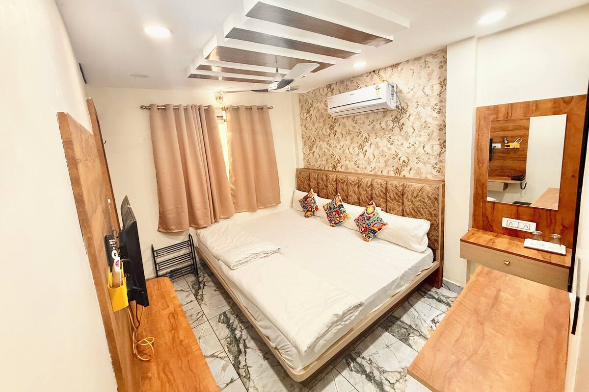 A hotel room with a large bed, a wooden headboard, a marble-tiled floor, a ceiling fan, and an air conditioning unit.