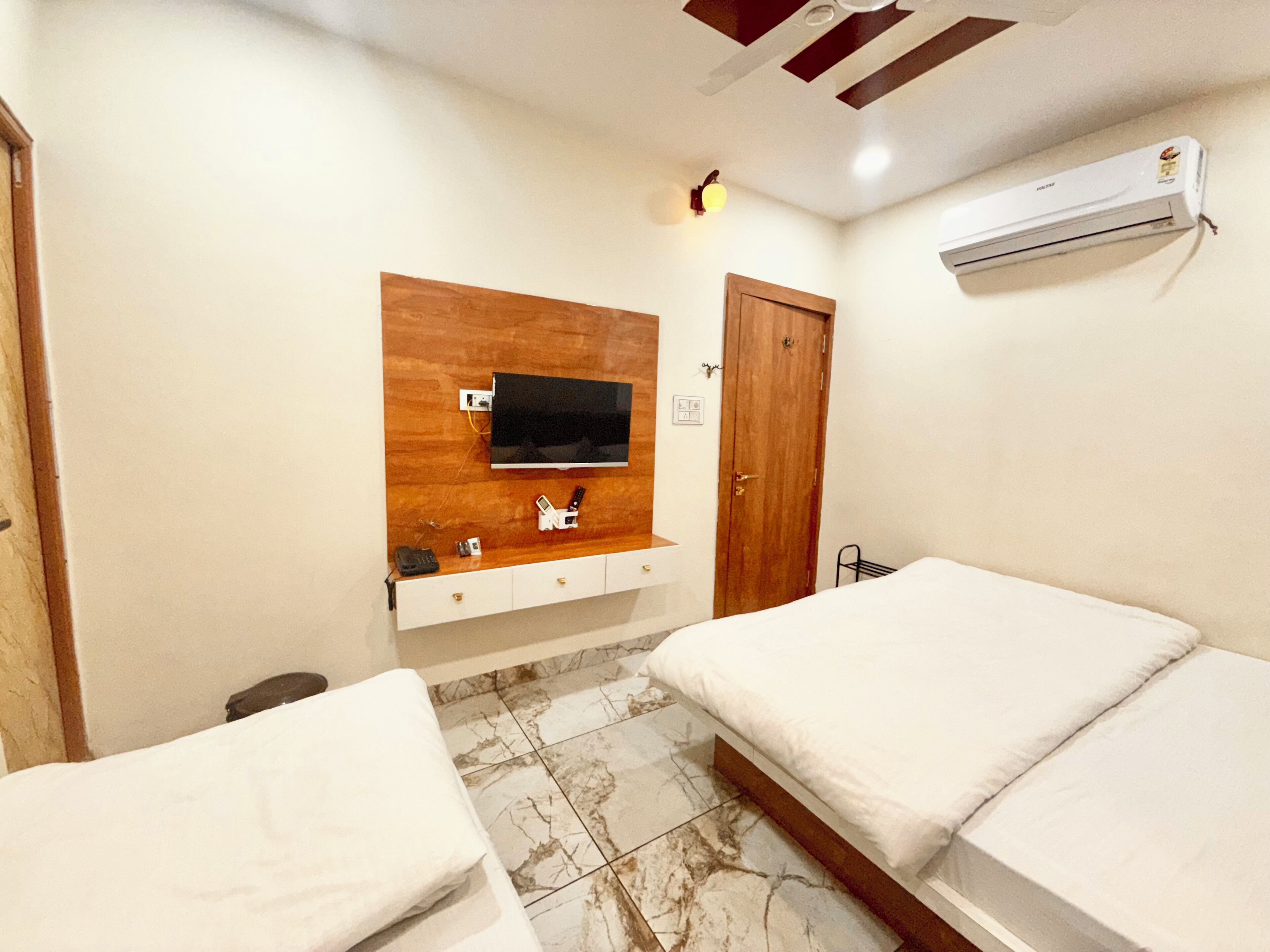 A hotel room with a wooden vanity, a flat-screen TV mounted on the wall, a door, and two beds.