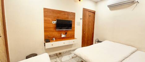 A hotel room with a wooden vanity, a flat-screen TV mounted on the wall, a door, and two beds.