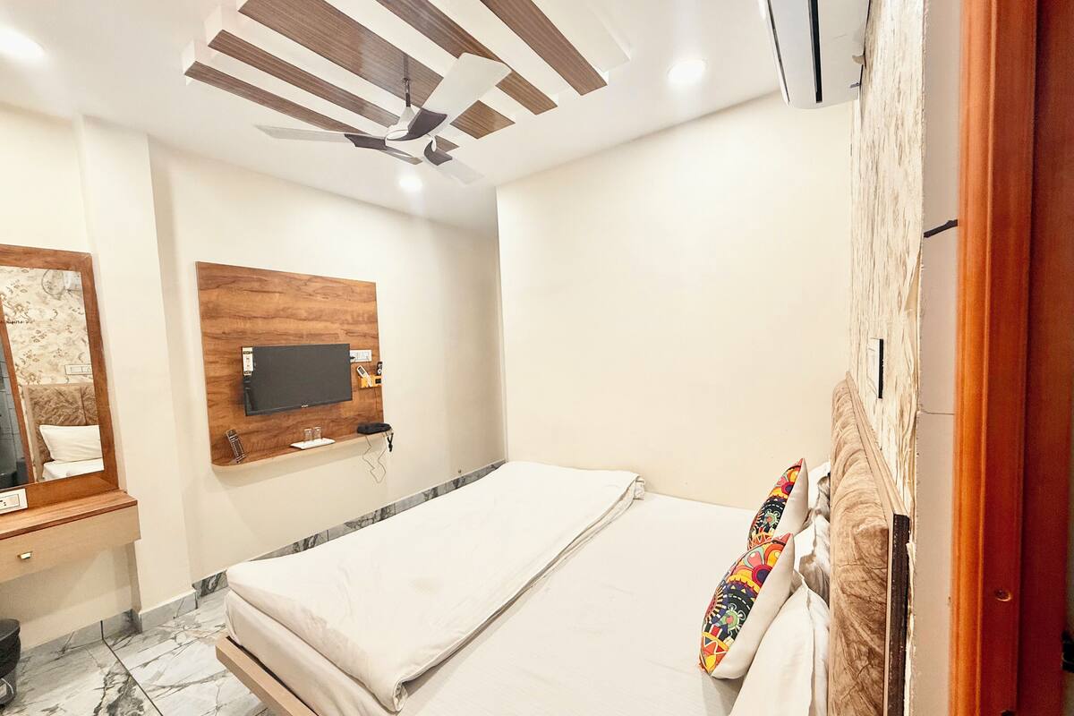 A bedroom with a bed, a TV mounted on a wooden panel, a ceiling fan, and a marble-tiled floor.