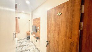 Un pasillo con una puerta de madera identificada con el número 203, suelo de baldosas de mármol, un pequeño banco de madera y un televisor montado en la pared.