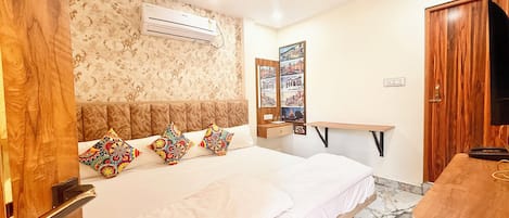 A modern bedroom with a large bed, a wooden headboard, a ceiling fan, an air conditioning unit, a wooden desk, and a television.
