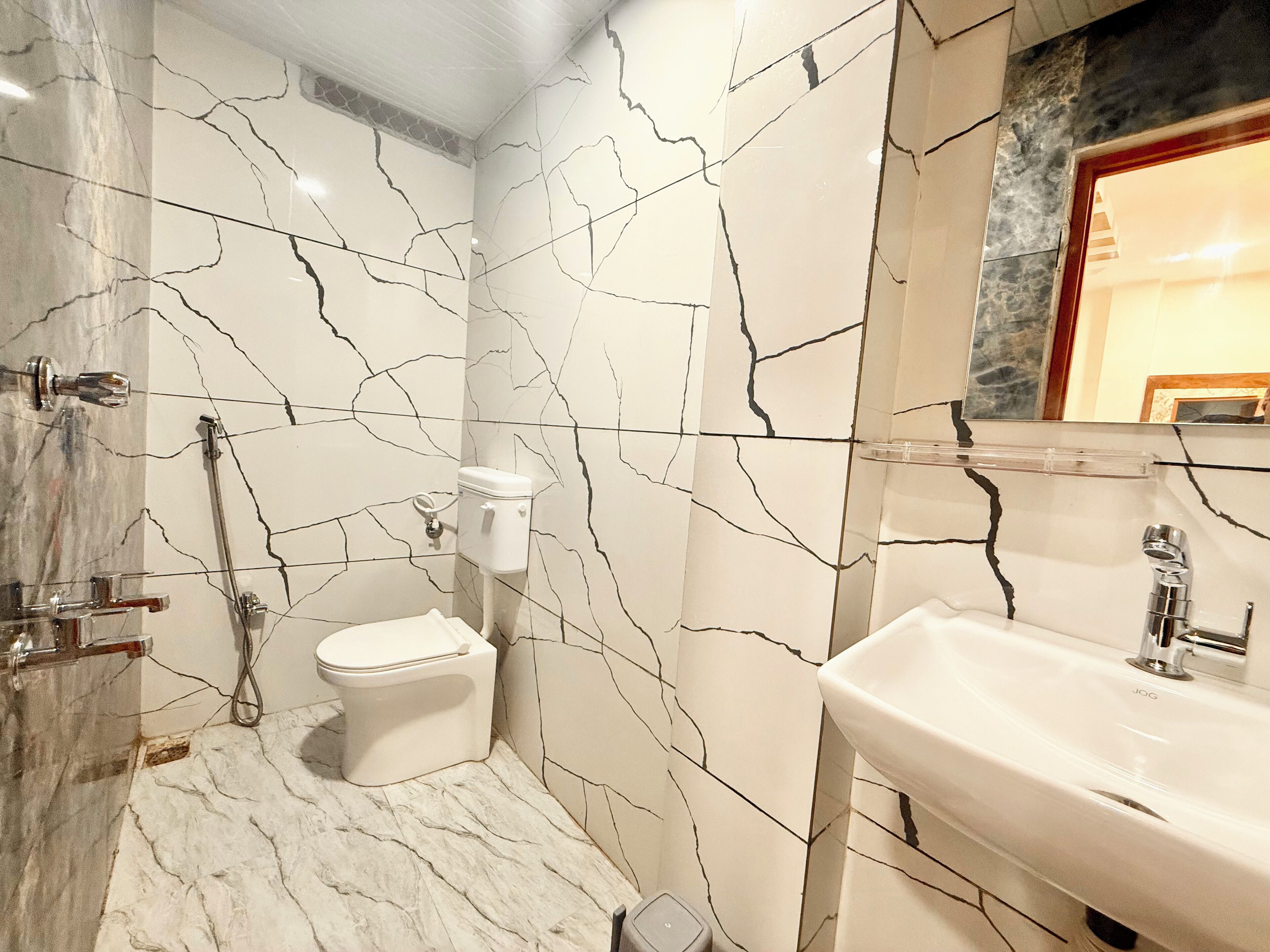 A bathroom with white marble walls and floor, a toilet, a sink, and a shower.