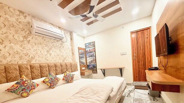 Habitación de hotel con cama, cabecera de madera, aire acondicionado de pared, armario de madera, televisor y una mesita con espejo.