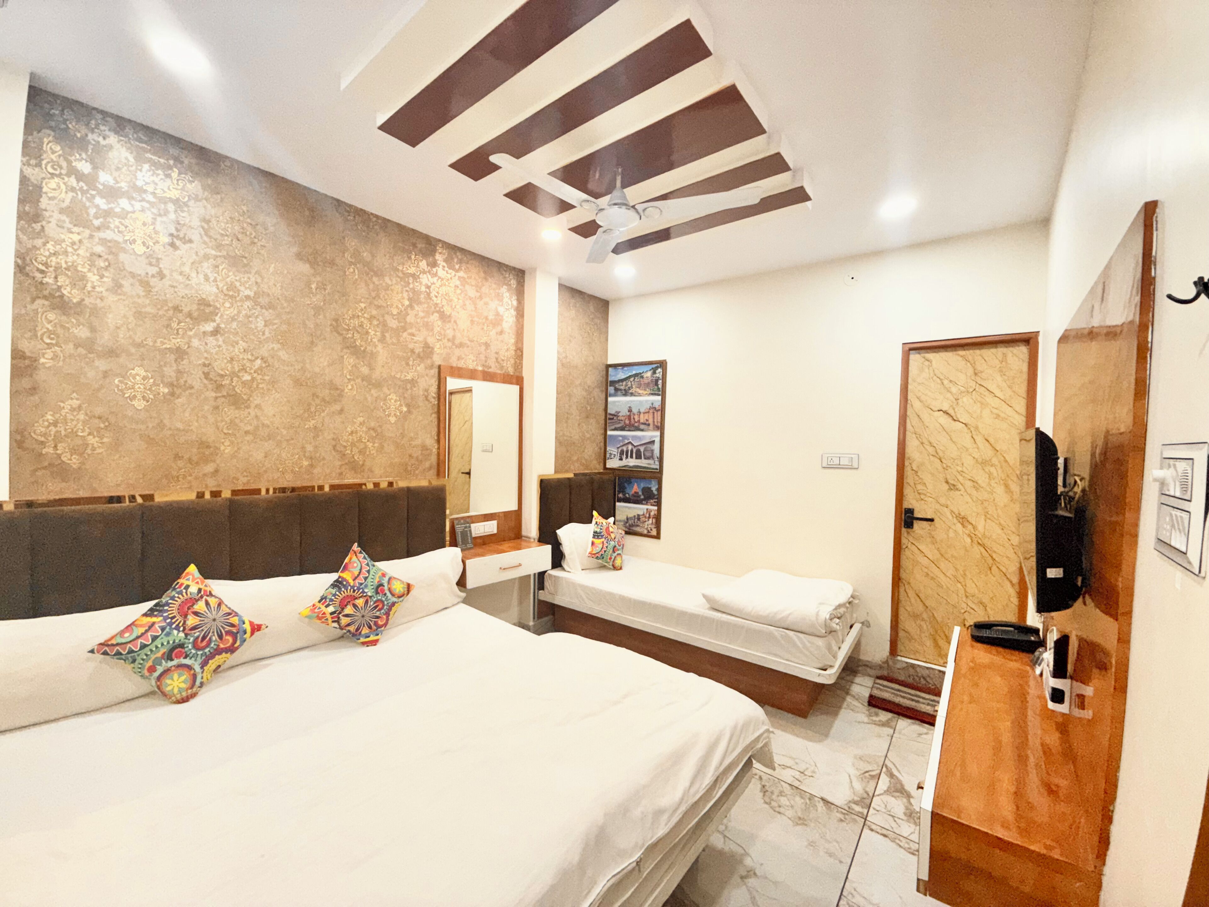 Habitación de hotel con una cama grande, una cama más pequeña, una tocador con espejo y una puerta con perchero.