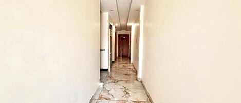 A corridor with marble flooring and white walls, leading to a door at the end.