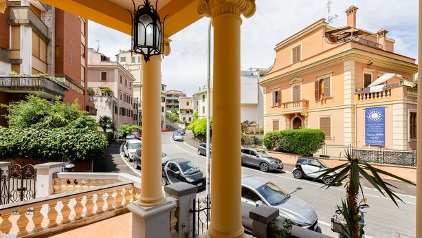 Un balcón con columnas amarillas, vista a la calle y un edificio con un letrero azul.