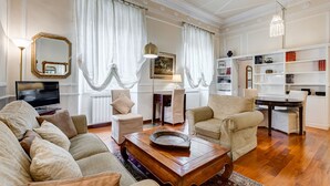 Amplia sala de estar con un sofá grande, una mesa de centro y una chimenea. Hay cortinas, un televisor y una estantería en la habitación.
