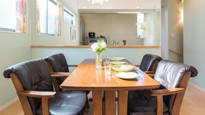 Un comedor con una mesa de madera y sillas de cuero, un florero con flores, y una cocina al fondo.