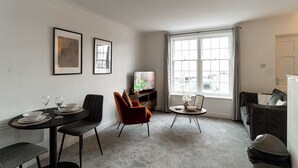 A living room with a dining table, two chairs, a sofa, a TV, and a window with curtains.