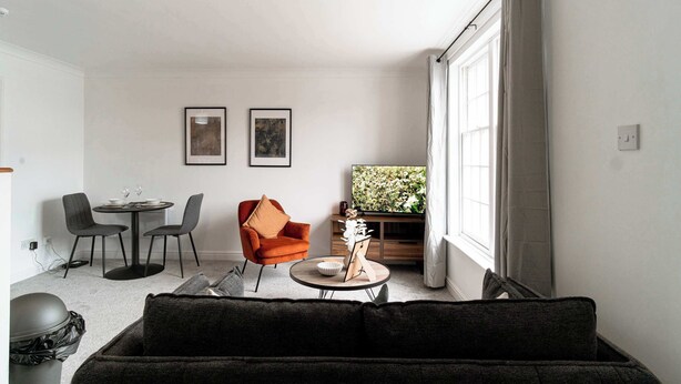 A modern living room with a sofa, a dining table with chairs, a TV, and artwork on the wall.
