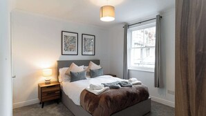 A bedroom with a bed, bedside table, lamp, artwork, and a window with curtains.