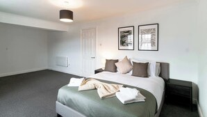 Une chambre d’hôtel avec un lit, une table de chevet, une commode, une porte et deux tableaux encadrés au mur.