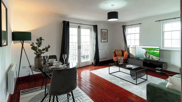 Un salon moderne comprenant un coin repas, un canapé, un téléviseur et offrant une vue sur un paysage verdoyant par les fenêtres.