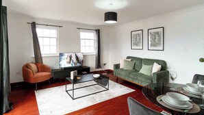 Un salon comprenant un canapé, une table basse, un téléviseur et un coin repas avec une table dressée pour deux personnes.