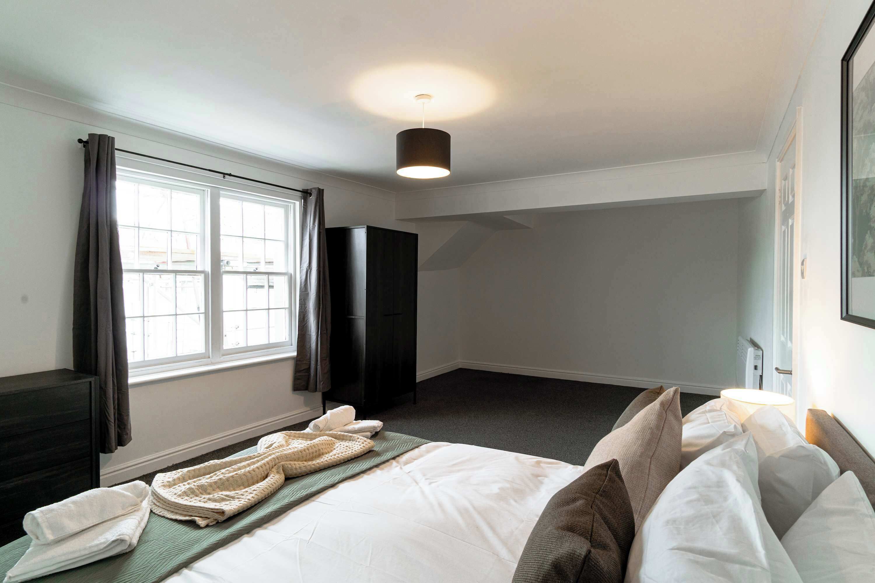Ein Hotelzimmer mit Bett, Schrank, Fenster mit Vorhängen und Deckenleuchte.