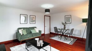 Un salon avec un canapé vert, une table basse, une table à manger avec des chaises et des tableaux encadrés accrochés au mur.