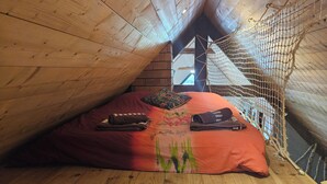 Un dormitorio acogedor en el ático, con techo inclinado, vigas de madera y ventana con mosquitero.