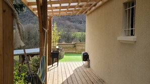 Una terraza de madera con una pérgola, una mesita y una hamaca colgante.