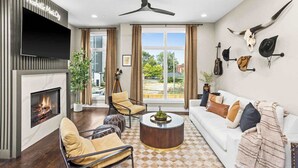A modern living room with a fireplace, a ceiling fan, and a view of the outdoors. - Gated Luxury in Nashville: Rooftop Views+Fire Pit (Nashville)