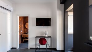 Une chambre d’hôtel moderne équipée d’un lit, d’un bureau avec une chaise, d’un téléviseur à écran plat et d’une salle de bain visible à travers une porte ouverte.