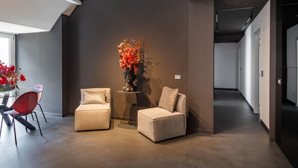 Un salon moderne comprenant un canapé, deux fauteuils, une petite table ornée d’un vase de fleurs et une table basse en verre.