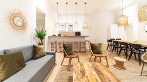 A modern living room with a grey sofa, wicker chairs, a wooden dining table, and a kitchen area with bar stools. - Smartstay - Suites Opera Barbara 3CH/8P (Lyon)