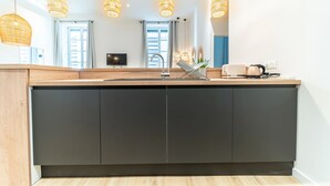 A modern kitchen with a central island, pendant lights, and a flat-screen TV. - Smartstay - Suites Opera Barbara 3CH/8P (Lyon)