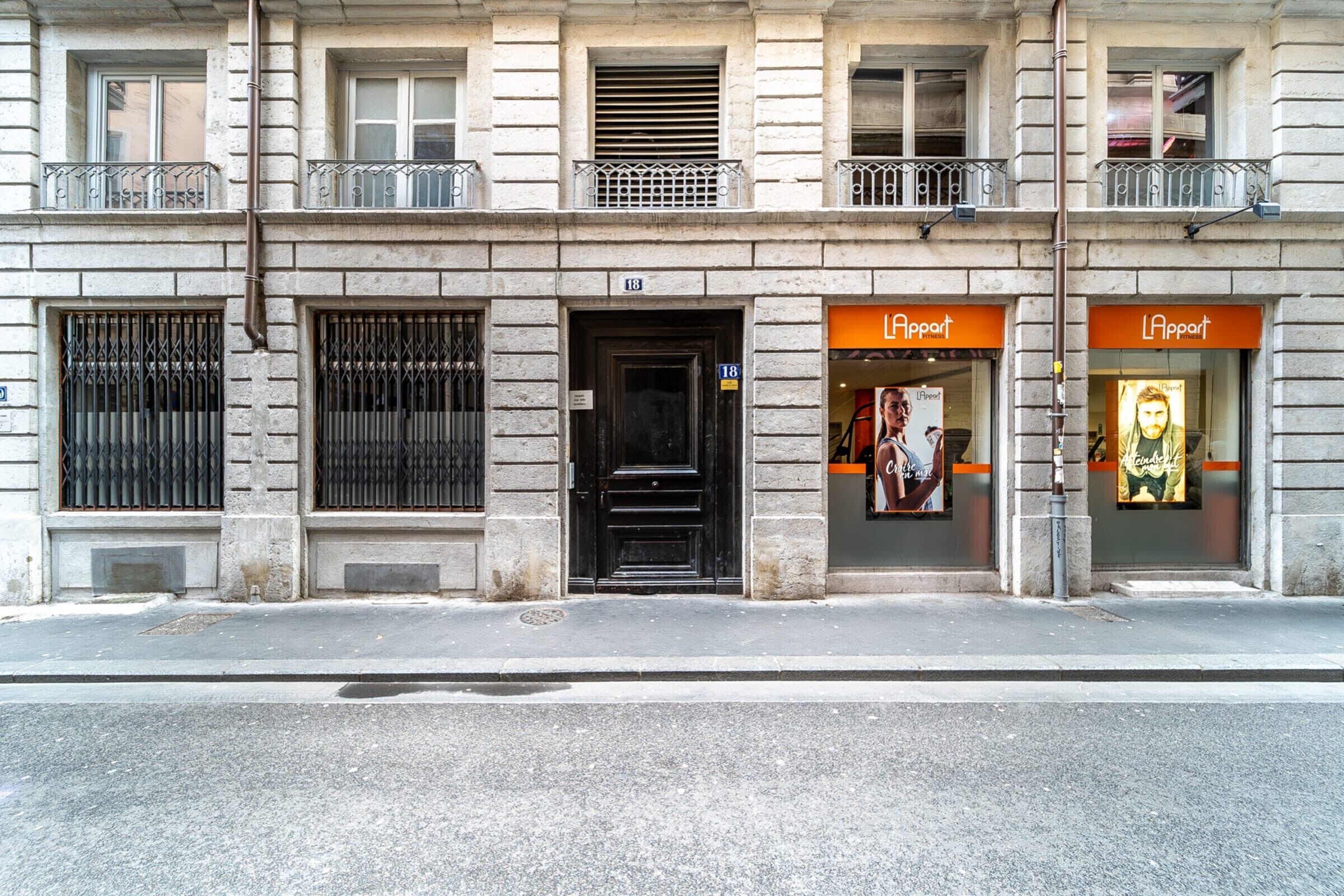 Un bâtiment avec une porte noire, deux fenêtres avec des barreaux en métal et un balcon doté d’une balustrade.