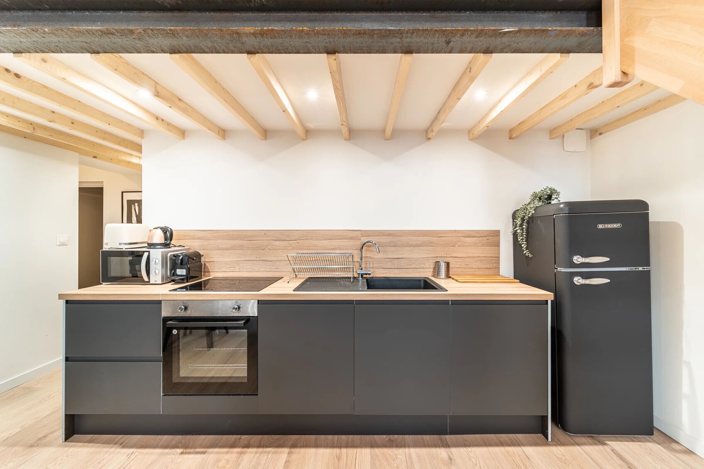 Eine moderne Küche mit Einbauofen, Spüle und einem schwarzen Kühlschrank.