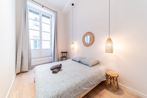 Ein Schlafzimmer mit einem Bett, zwei Pendelleuchten, einem runden Spiegel und einem hölzernen Hocker.
